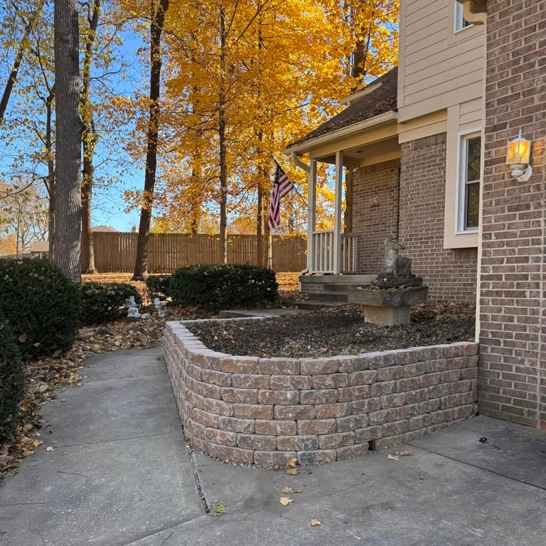 Curved stacked-block retaining wall built along a brick home's front walkway, holding back a raised planting bed.