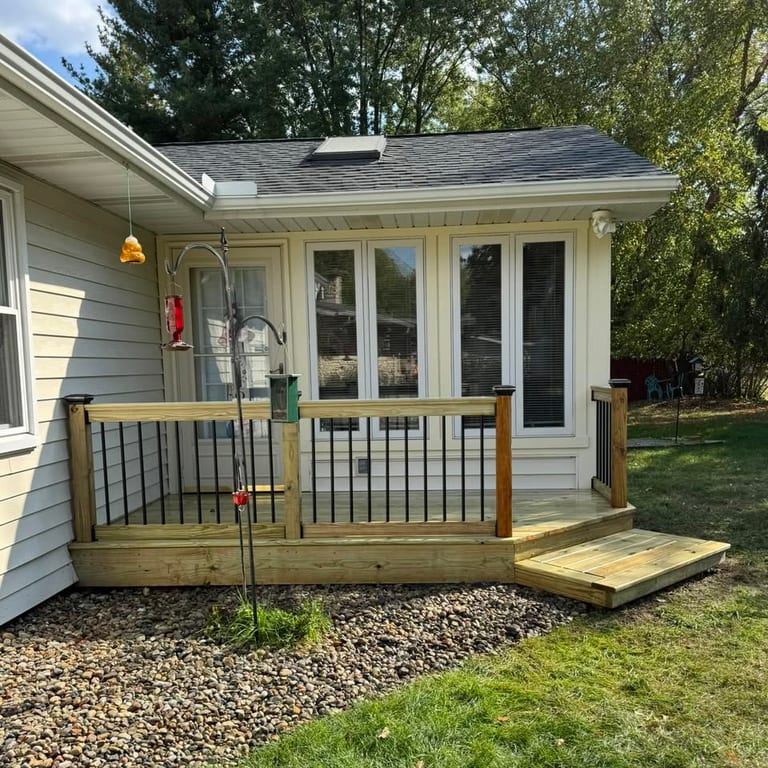 Pressure-treated wood deck with black metal balusters and a wide step, built onto the back of a ranch home by Mercer Precision Construction.