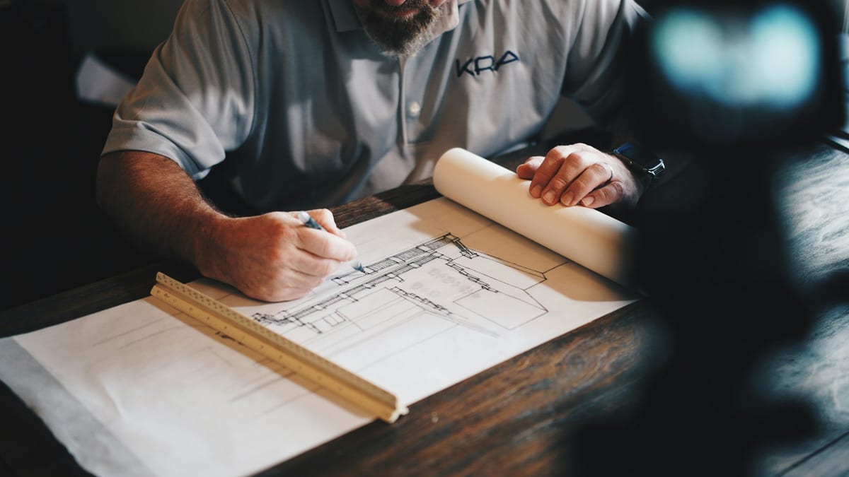 A contractor sketching project plans on paper with a folding ruler alongside.