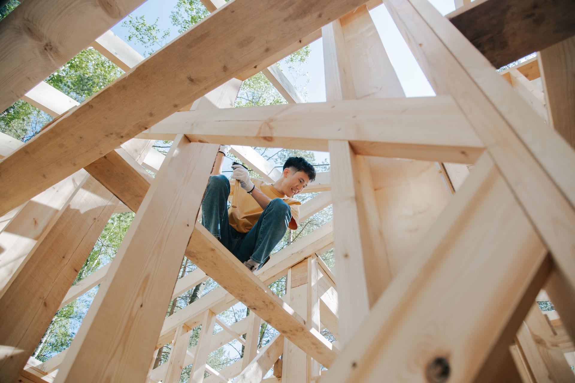 Carpenter fastening timber framing members together on a residential build under a clear sky.